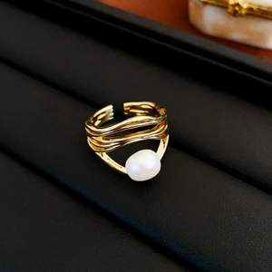 Detail of minimalist gold wavy ring with single white pearl on a black leather tray
