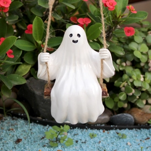 Detail of cute white ghost figurine on a wooden swing hanging in a blooming garden