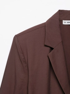 Close-up of dark brown blazer fabric showing textured weave and high-quality stitching