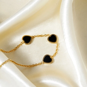 Elegant gold heart bracelet with three black pendants on a soft white silk background
