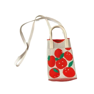 Detail of knitted mini bag featuring red strawberry patterns and woven shoulder strap