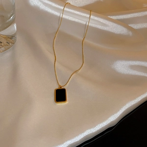 Dettaglio di una collana con ciondolo rettangolare dorato su sfondo di seta con luce calda