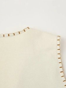 Detail of cream sleeveless top featuring textured fabric and brown contrast stitching
