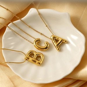 Macro shot of gold balloon-style letter pendants on a white shell dish and silk background
