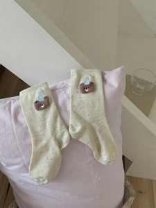 Detailed embroidery of a cartoon bear with a blue party hat on beige spotted socks