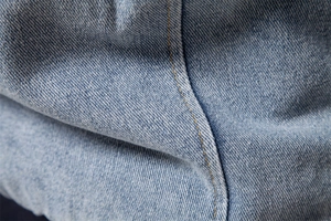 Detailed macro shot of light blue denim fabric with reinforced yellow stitching seams
