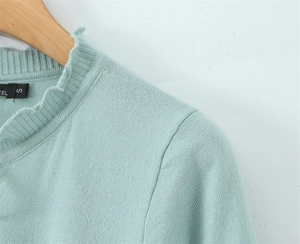 Dettaglio di maglia in maglina verde menta con collo a volant su gruccia in legno