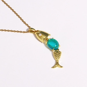 Detail of creative gold plated fish necklace with blue gemstone and white pearl accent