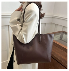 Macro side view of a large brown leather tote bag worn by a model in a minimalist setting