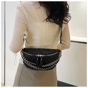 Close-up of black quilted waist bag featuring golden chains and dual zippers on a model