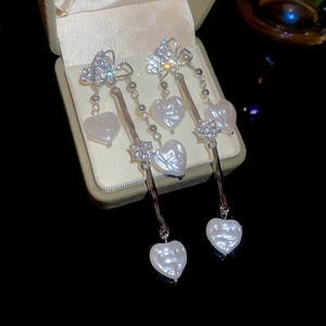 Détail de boucles d'oreilles pompon en argent avec nœud diamant et cœurs de perle