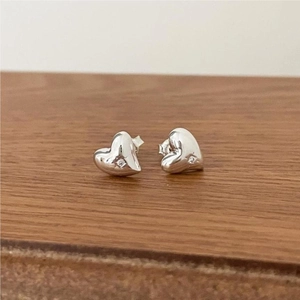 Close-up of minimalist heart-shaped silver earrings on a warm brown wooden surface