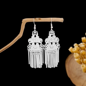 Detail view of silver tassel earrings with ethnic hollow patterns on a wooden branch