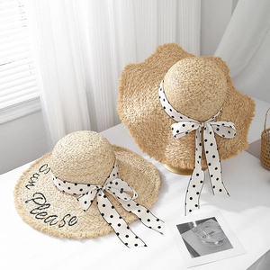 Close-up of raffia sun hat with Sun Please embroidery and polka dot ribbon bow detail