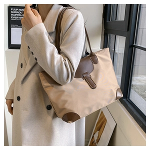 Detailed side view of khaki nylon tote bag with brown leather trim worn by model