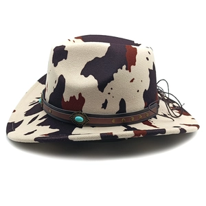 Detail of cow print cowboy hat featuring a leather band with turquoise stone and metal studs