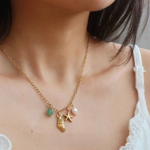 Close-up of gold starfish and shell pendants with pearl on a stainless steel necklace
