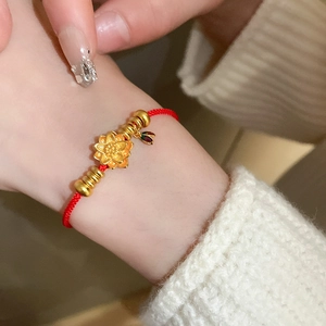 Détail du bracelet en cordon rouge tressé avec pendentif lotus doré porté au poignet