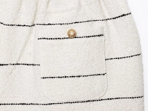 Dettaglio ravvicinato del tessuto tweed bianco a righe nere con bottone dorato decorativo