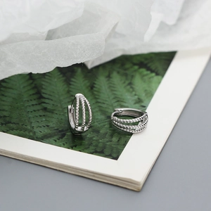 Macro view of triple-layered twisted silver hoop earrings on a decorative leaf card