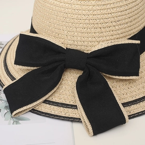 Primo piano di un cappello di paglia da donna con un grande fiocco in tessuto nero e trama fitta