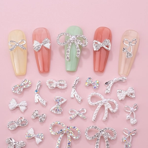 Silver alloy bow nail charms with rhinestones and pearls displayed on pink background