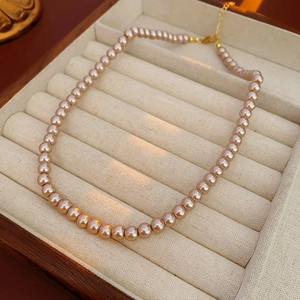 Detail of elegant champagne pearl necklace with gold clasp in a beige velvet jewelry box