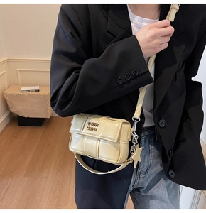 Gros plan du sac bandoulière tissé crème avec chaîne dorée sur une veste de blazer noir