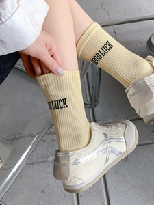 Close-up of knit crew socks with Good Luck print and stylish sneakers on grey floor