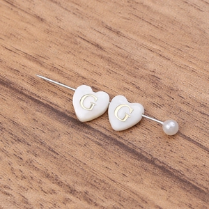 Détail macro de perles en nacre en forme de cœur avec lettre G dorée pour bijoux DIY