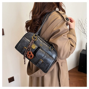 Detail of vintage black leather tote bag with pocket buckles and pretzel charm