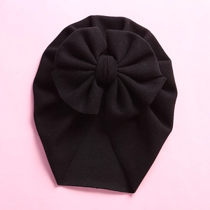 Close-up of a black baby turban hat with a large bow detail on a pink background