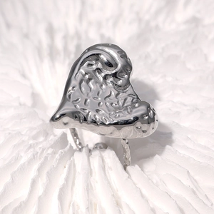 Macro shot of silver heart ring with unique hammered texture on a wavy white background