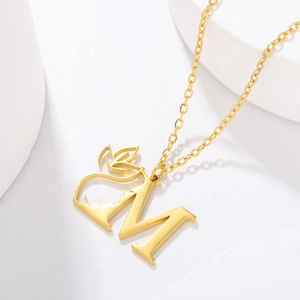 Macro detail of a gold letter M necklace with leaf motifs and a polished cross chain