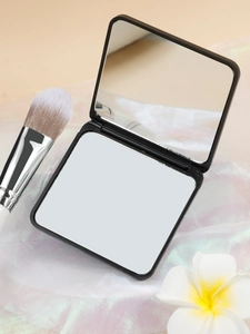Close-up of black square folding makeup mirror with makeup brush on soft fabric
