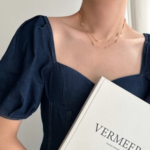 Close-up of a layered gold plated stainless steel bead necklace on a model wearing denim