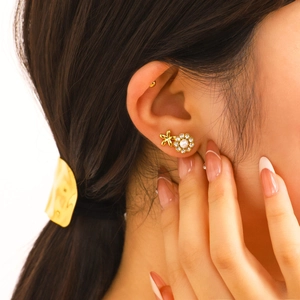 Elegant gold flower stud earrings with pearl center and crystals on a female model