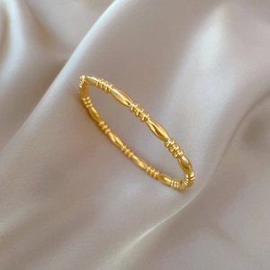 Minimalist gold titanium steel beaded bracelet on champagne silk fabric background