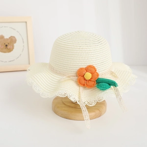 Detail of cream straw hat featuring orange knitted flower and delicate lace brim