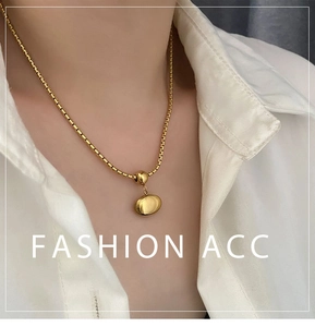 Detail shot of a minimalist gold bean pendant necklace on a white box chain style