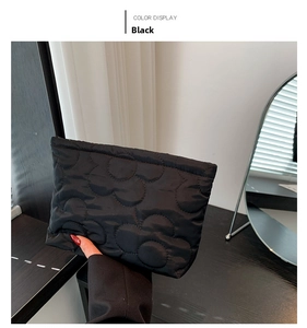 Detail view of a black quilted makeup bag with floral stitching held by a model