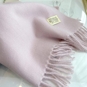 Close-up of pink cashmere-like scarf showing soft texture, fringe edge and woven tag