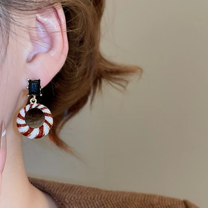 Macro side view of a model wearing festive round pendant earrings with red spiral patterns