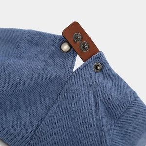 Detail of blue knit hat featuring brown leather strap with metal snap buttons