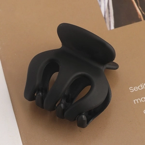Macro detail of matte black hair claw clip with cross-tooth design on a magazine
