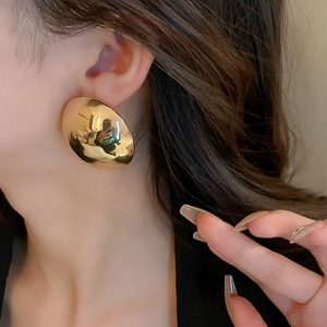 Close-up of a large gold polished disc earring on model, showing bold metallic texture