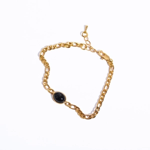 Detail of a 14K gold Figaro chain bracelet with a black oval gemstone and lobster clasp