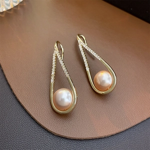 Elegant gold teardrop earrings with champagne pearls and sparkling crystals on brown leather