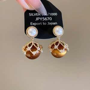 Close-up of 18K gold plated pearl and tiger eye earrings with intricate metal filigree