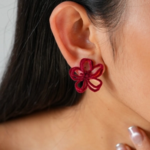 Gros plan de boucles d'oreilles fleurs floquées rouge foncé sur une oreille
